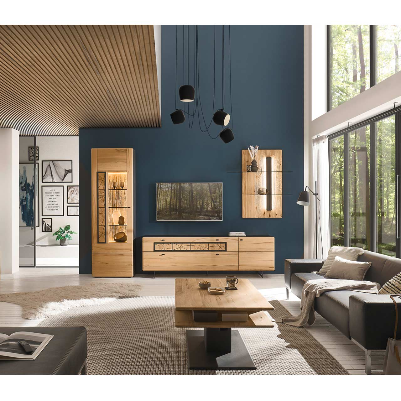 Modern eingerichtetes Wohnzimmer mit dreiteiliger Wohnwand aus Kernbuche: Standvitrine, Lowboard auf Metallkufen und Wandpaneel. Im Vordergrund passender Couchtisch neben grauer Couch.
