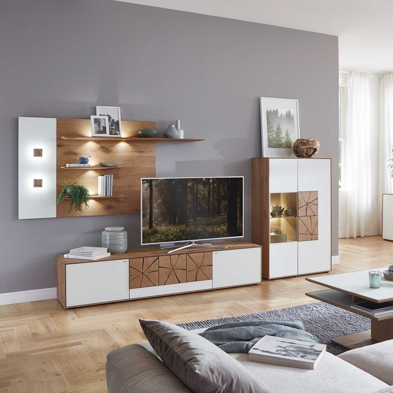 Wohnzimmer mit moderner Massivholz Wohnwand mit Mattglas weiß Fronten und dekorativen Hirnholzscheiben: Langes Lowboard mit Hirnholz, Wandpaneel mit zwei Regalböden und Highboard mit beleuchtetem Glasausschnitt und Hirnholz.