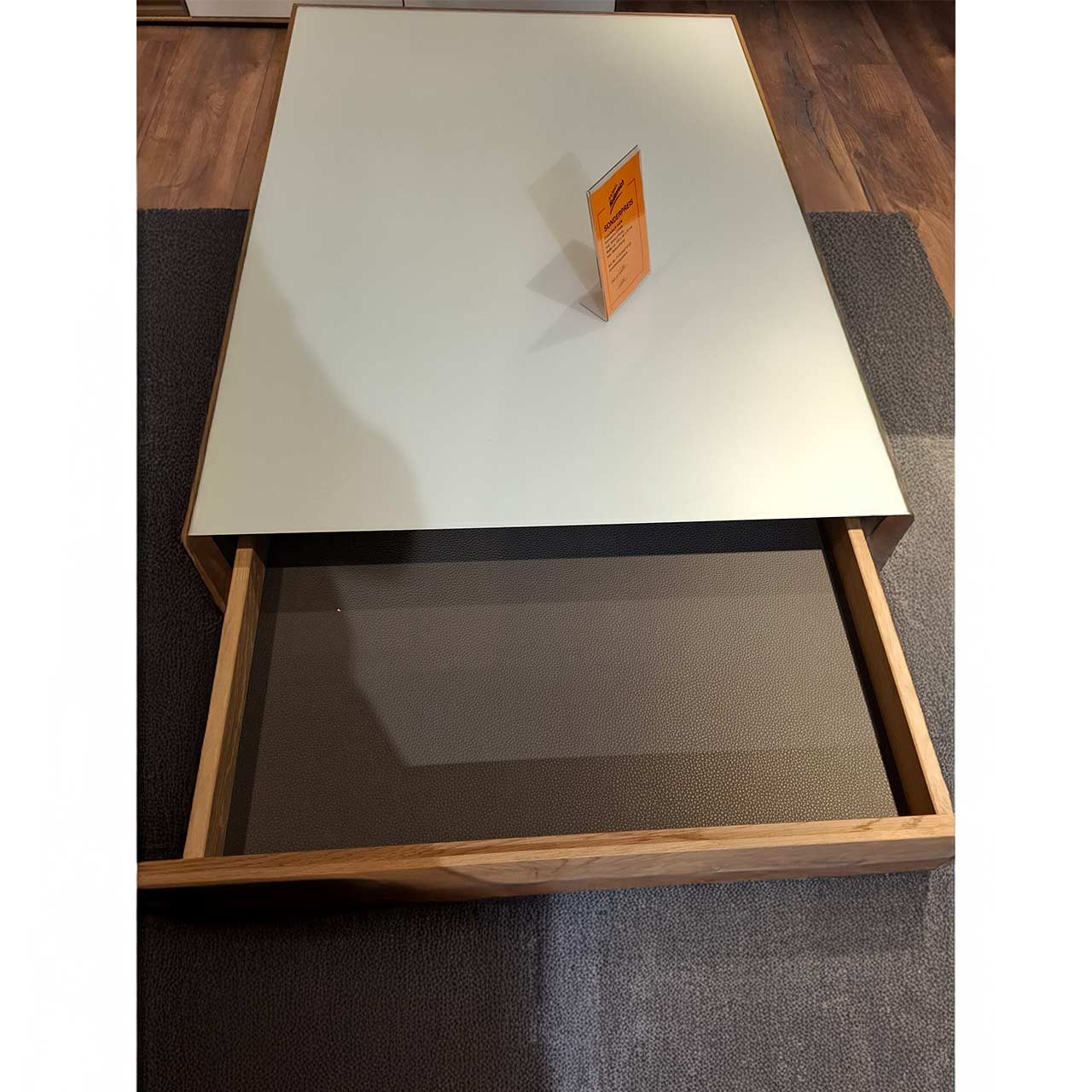 Moderner, rechteckiger Couchtisch aus massiver Kerneiche. Dicke Tischplatte in Mattglas weiß mit integriertem, geöffnetem Schubkasten und seitlichem Ablagefach.