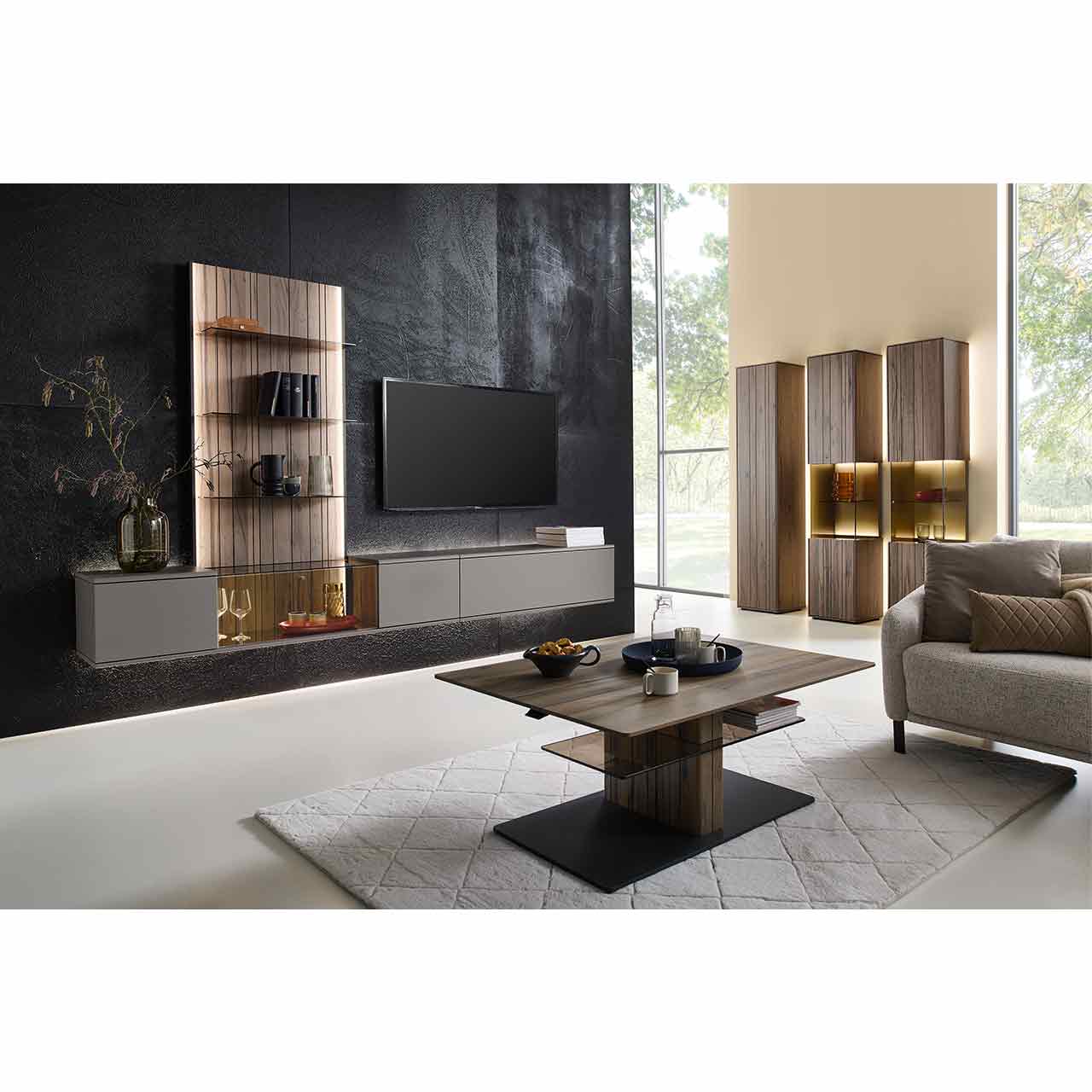 Modernes Wohnzimmer mit Wohnwand bestehend aus sandfarbenen Hängelowboards und beleuchtetem Wandpaneel aus Altholzbuche mit Glasböden. Davor rechteckiger Couchtisch, rechts an der Wand drei passende Standvitrinen.