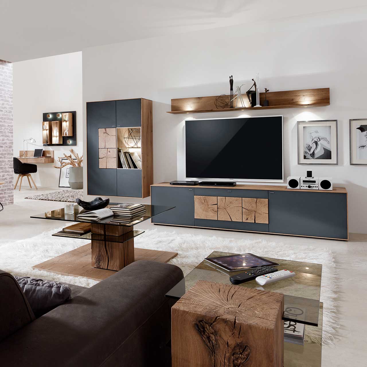 Wohnzimmer mit moderner dreiteiliger Massivholz Wohnwand mit Mattglas Anthrazit Fronten und dekorativen Hirnholzscheiben: Lowboard mit Hirnholz, Wandregal mit Spotbeleuchtung, große Hängevitrine mit beleuchtetem Glasausschnitt und Hirnholz.