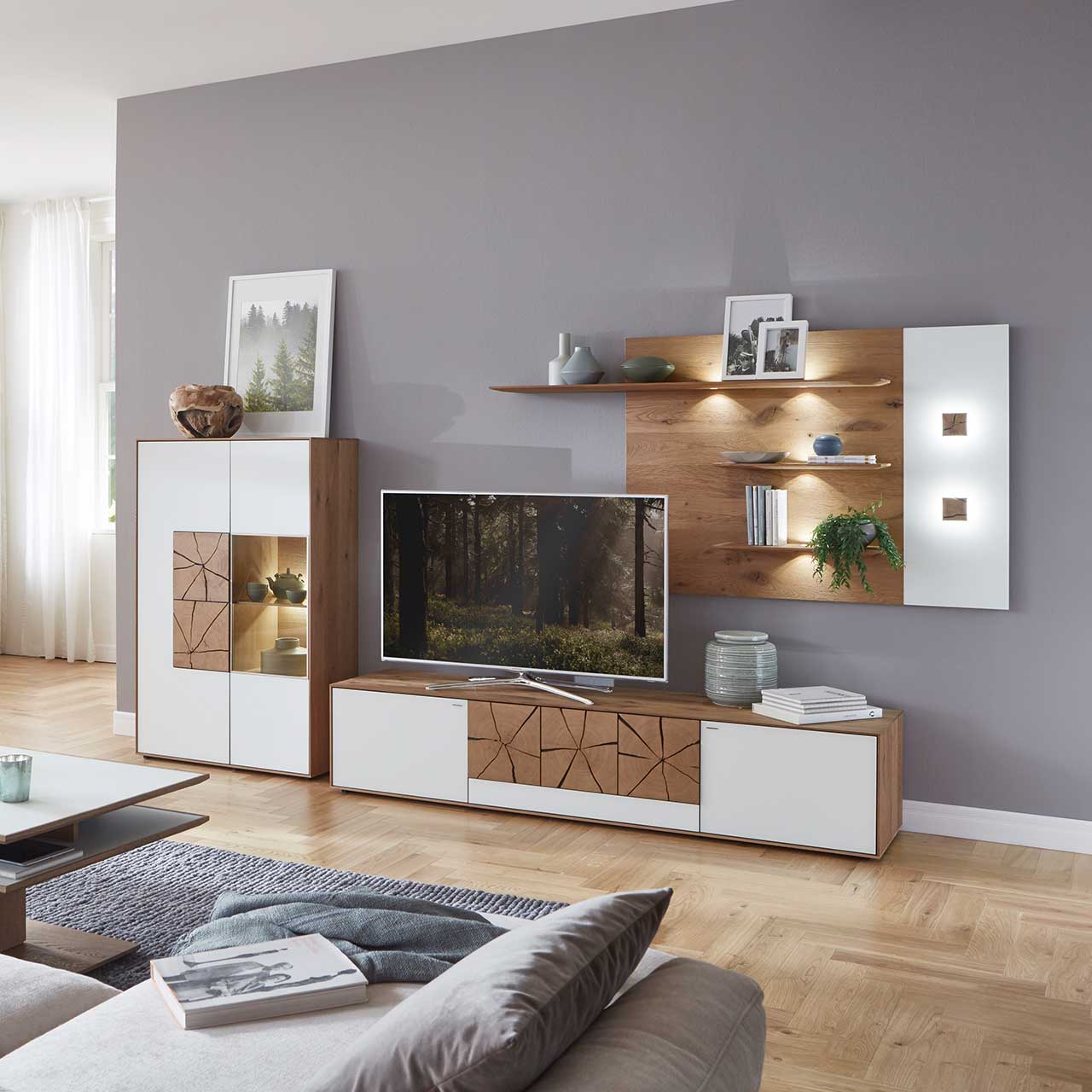 Wohnzimmer mit moderner Massivholz Wohnwand mit Mattglas weiß Fronten und dekorativen Hirnholzscheiben: Langes Lowboard mit Hirnholz, Wandpaneel mit zwei Regalböden und Highboard mit beleuchtetem Glasausschnitt und Hirnholz.