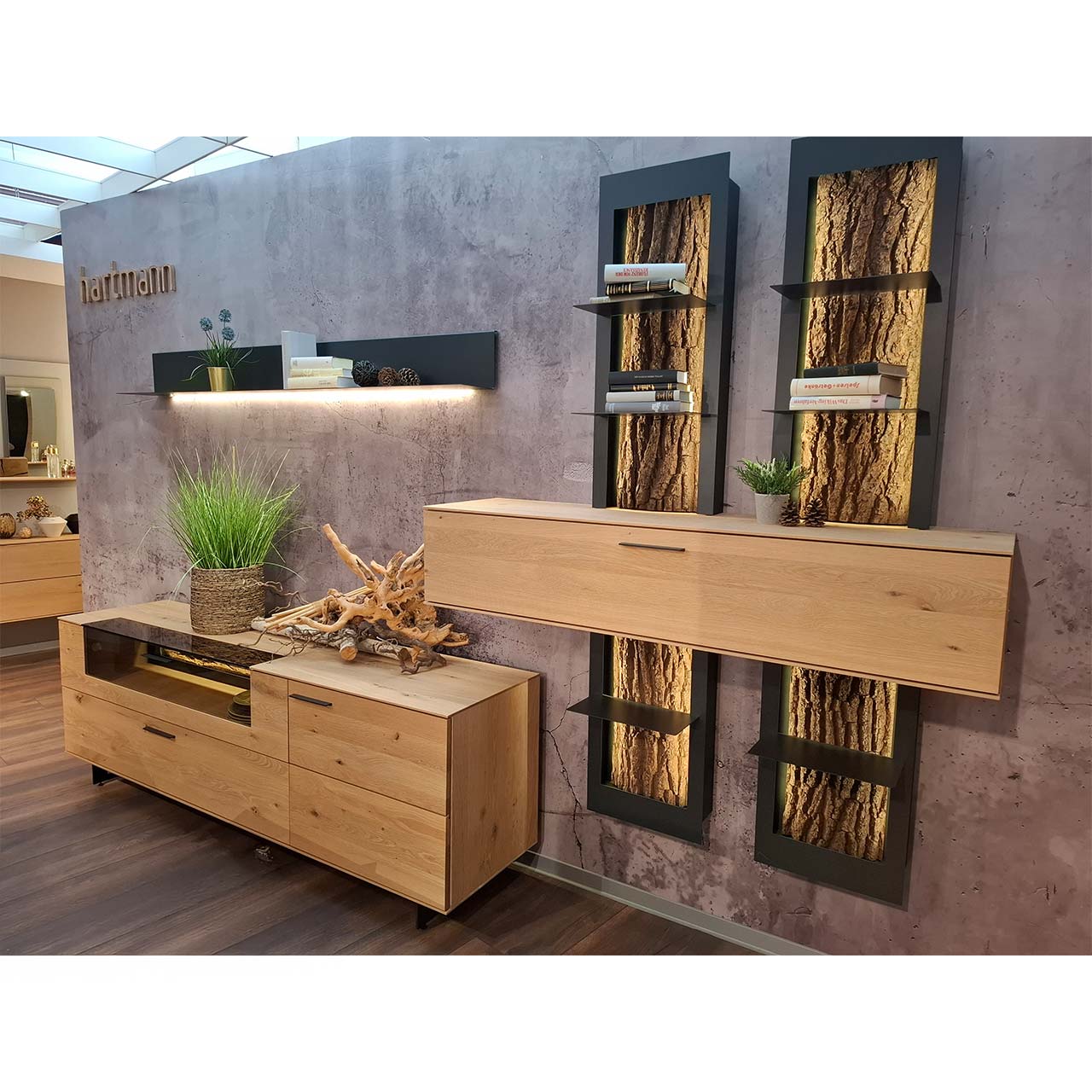 Moderne sechsteilige Wohnwand aus massiver Kerneiche und echter Baumrinde: Lowboard auf Metallkufen mit Glasausschnitt, Klappe und Schubkasten, beleuchtetes Metallpaneel, Hängeschrank aus Holz eingefasst in zwei Regalelemente aus Metall mit Baumrinde.