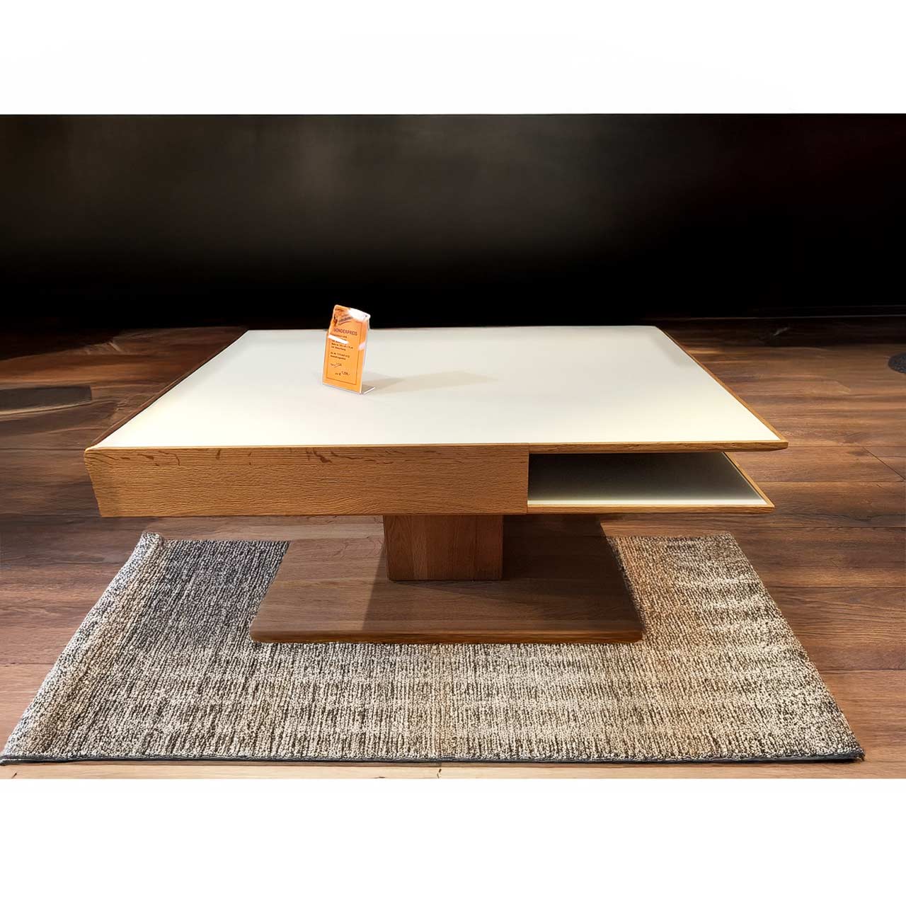 Moderner, rechteckiger Couchtisch aus massiver Kerneiche Umato. Dicke Tischplatte in Mattglas weiß mit integriertem Schubkasten und seitlichem Ablagefach, auf massiver, rechteckiger Holzsäule und Bodenplatte stehend.