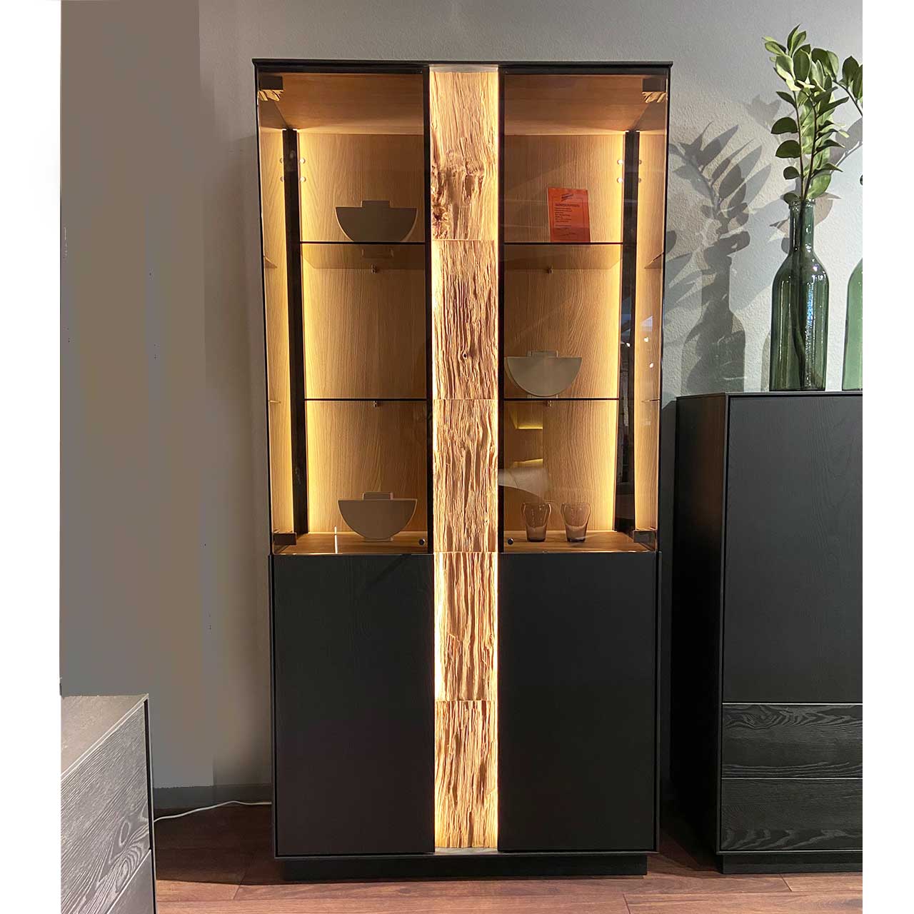 Hartmann SALE Möbel - KILVA Standvitrine 9610-0091 - inkl. Beleuchtung / Originalbild Ausstellung Moderne Standvitrine aus anthrazitfarbener Kernesche mit Holz,- Glastüren, beleuchteter Rückwand mit Glasböden und mittigem beleuchtetem Spaltholz-Akzent.