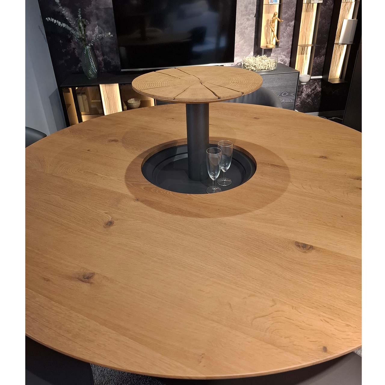 Detailaufnahme eines ausfahrbaren Flaschenfaches, integriert in der Mitte des Holztisch der Möbelserie NATURZEIT Nr. 1557. Deckel des Faches ist aus Holz in From einer runden Hirnholzplatte.