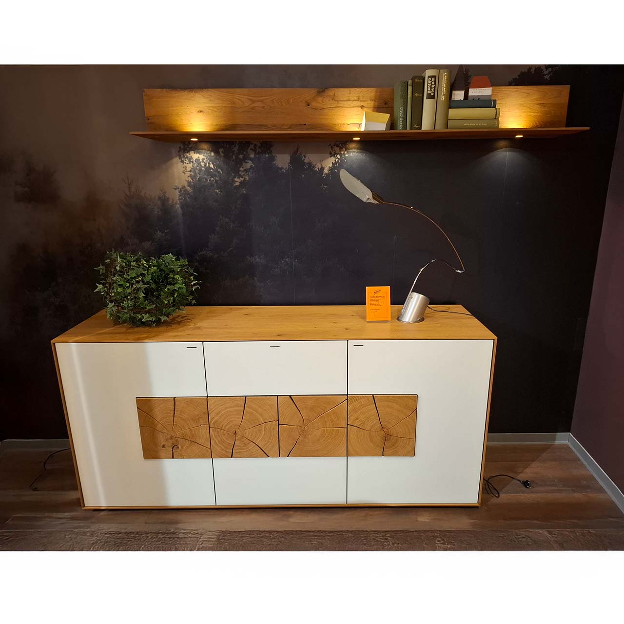 Möbel ZweierSet: Ein modernes Sideboard aus massiver Kerneiche Umato mit weißfarbenen Mattglasfronten und vier dekorativen, rechteckigen Hirnholzscheiben und ein Wandpaneel aus massivem Holz mit Ablageboden und Spotbeleuchtung.