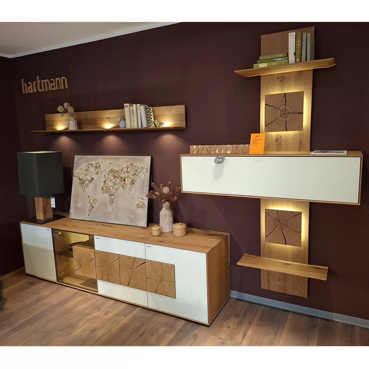 Hartmann SALE Möbel - CAYA Wohnwand 7170 Nr. 60W vierteilig - inkl. Beleuchtung / Originalbild Ausstellung Moderne vierteilige Massivholz Wohnwand aus Kerneiche Umato mit Mattglas weiß Fronten: Lowboard mit Glasausschnitt und Hirnholz, Wandregal aus Holz, schlichter Hängeschrank eingefasst in ein Holzwandpaneel mit Ablageböden.