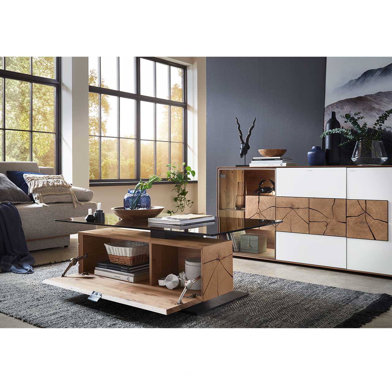 Milieubild Wohnzimmer - Hartmann NATURWERKE - Couchtisch 7100C-0481 - offen Couchtisch mit rechteckiger Glasplatte und Hirnholzblock aus massiver Kerneiche mit offener Klappe mit Blick ins Stauraumfach. Dahinter passendes Sideboard mit weißer Front und Hirnholzscheiben - im Wohnzimmer stehend.