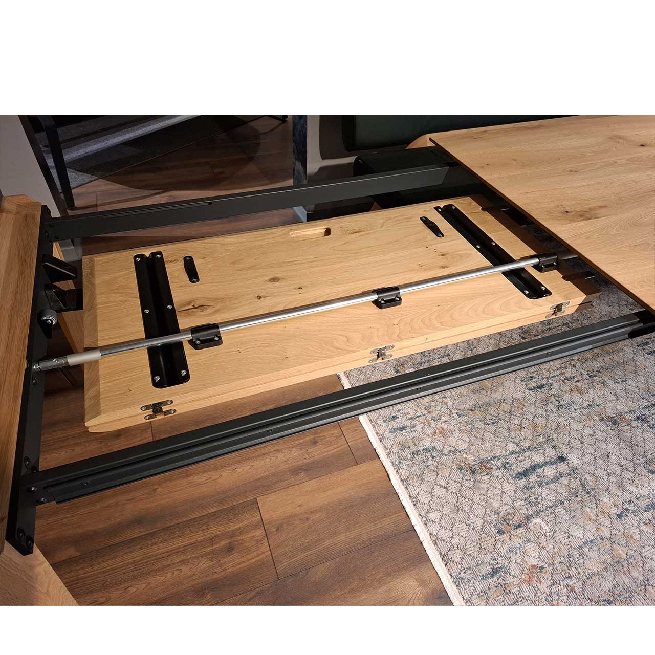 Detailansicht des integrierten, zusammengeklappten Tischauszugs in der Tischplatte des Esstisches Nr. 8400E-1807 aus massiver Kerneiche Natur; der Mechanismus befindet sich am linken Tischkopf.